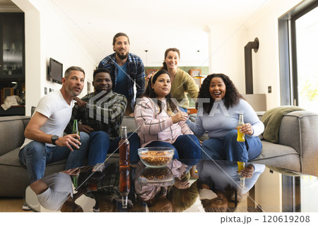 Happy diverse male and female friends watching sport on tv at home and drinking beers, copy space Happy diverse male and female friends watching sport on tv at home and drinking beers, copy space 120619208