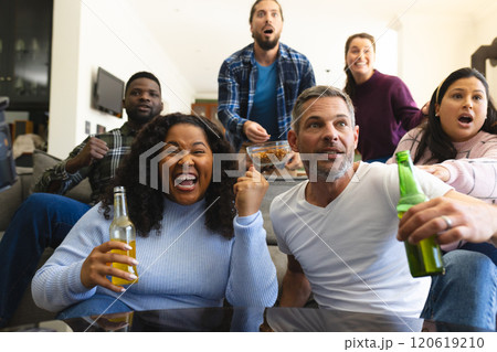 Excited diverse male and female friends watching sport on tv at home and drinking beers, copy space Excited diverse male and female friends watching sport on tv at home and drinking beers, copy space 120619210