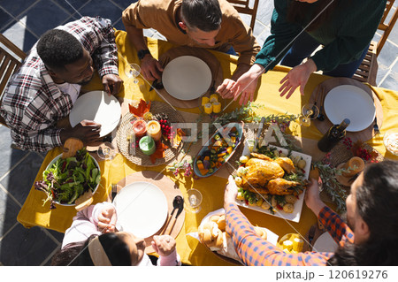 Happy diverse male and female friends serving thanksgiving celebration meal in sunny garden 120619276
