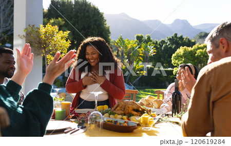 Happy diverse male and female friends serving thanksgiving celebration meal in sunny garden 120619284