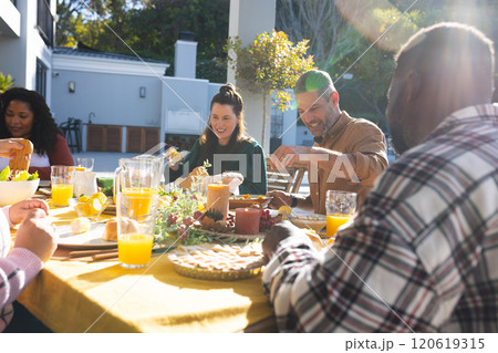 Happy diverse male and female friends eating thanksgiving celebration meal in sunny garden 120619315