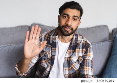 Happy biracial man sitting on sofa, having video call and waving hand in living room at home Happy biracial man sitting on sofa, having video call and waving hand in living room at home 120619363