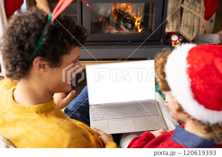 Diverse gay male couple wearing christmas hats and having laptop video call at home, copy space 120619393