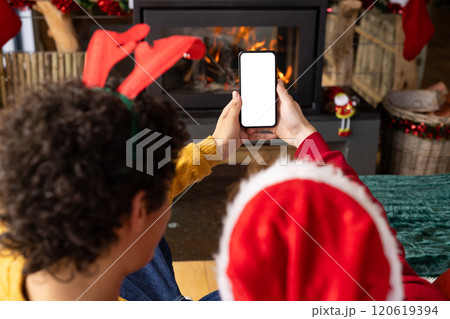 Diverse gay male couple wearing christmas hats and having smartphone video call at home, copy space 120619394