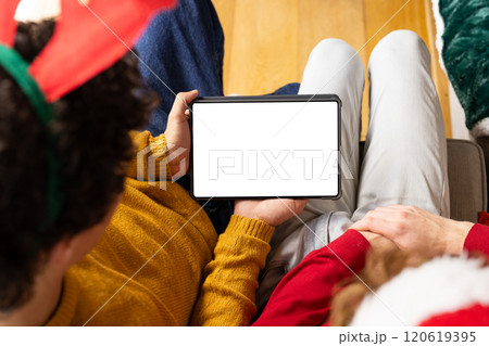 Diverse gay male couple wearing christmas hats and having tablet video call at home, copy space Diverse gay male couple wearing christmas hats and having tablet video call at home, copy space 120619395