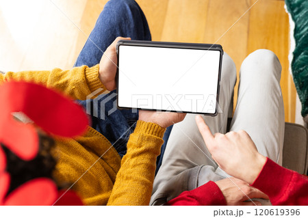 Diverse gay male couple wearing christmas hats and having tablet video call at home, copy space 120619396