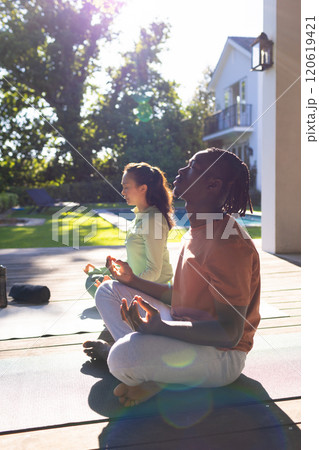 Happy diverse couple practicing yoga meditation sitting on deck in sunny garden, copy space 120619421