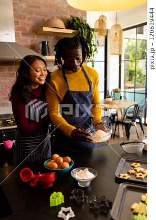 Happy diverse couple in aprons baking christmas cookies in kitchen, copy space Happy diverse couple in aprons baking christmas cookies in kitchen, copy space 120619444