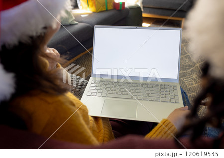 Diverse couple in christmas hats having laptop video call, copy space screen 120619535