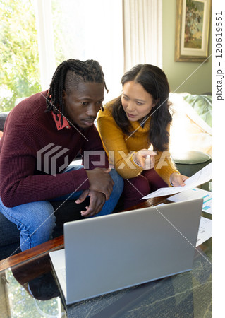 Serious diverse couple sitting on couch using laptop discussing bills and finances in living room Serious diverse couple sitting on couch using laptop discussing bills and finances in living room 120619551