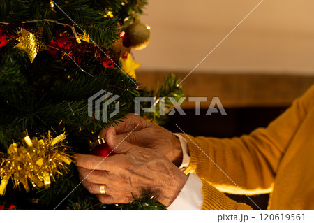 Caucasian senior woman decorating christmas tree in living room at home in evening 120619561