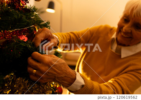 Happy caucasian senior woman decorating christmas tree in living room at home 120619562