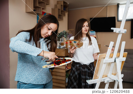 Two women painting together in a creative studio during daytime Two women painting together in a creative studio during daytime 120620488