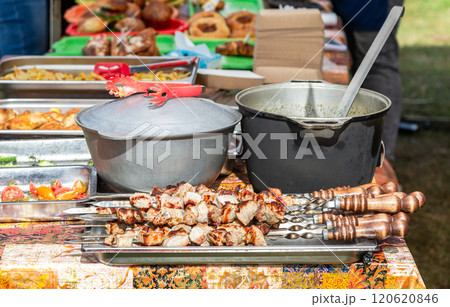 Appetizing hot shish kebab or shashlik on metal skewers, two metal cooking pots on the table outdoors 120620846