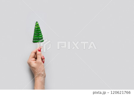Christmas tree shaped green lollipop in woman hand. Xmas creative minimal greeting card. View from above. Copy space Christmas tree shaped green lollipop in woman hand. Xmas creative minimal greeting card. View from above. Copy space 120621766