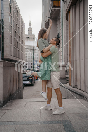 Happy couple of tourists walking embraced while sightseeing the town. Happy couple in front of palace of culture and science in Warsaw, Poland. Close up of a couple kissing. Happy couple of tourists walking embraced while sightseeing the town. Happy couple in front of palace of culture and science in Warsaw, Poland. Close up of a couple kissing. 120622291