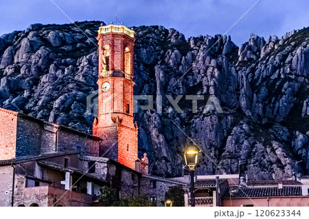 Views of the illuminated Church of Sant Corneli in Collbato, Barcelona at dusk, with the Montserrat mountain in the background 120623344