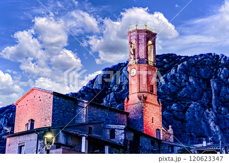 Views of the illuminated Church of Sant Corneli in Collbato, Barcelona at dusk, with the Montserrat mountain in the background 120623347