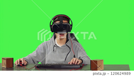 POV of person playing vr videogames sitting at desk over greenscreen backdrop, going online with friends enjoying rpg gameplay. Young adult using virtual reality headset, gaming. 120624989