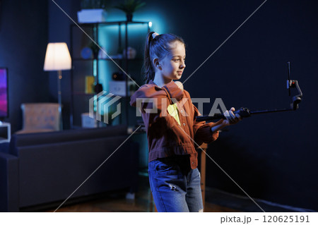 Kid in dimly lit studio joins viral dance craze, recording family friendly video with cellphone on selfie stick. Little girl in living room does latest internet dancing challenge, films with phone Kid in dimly lit studio joins viral dance craze, recording family friendly video with cellphone on selfie stick. Little girl in living room does latest internet dancing challenge, films with phone 120625191