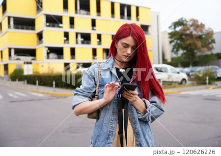 Young woman with red hair checks phone while walking through parking lot 120626226