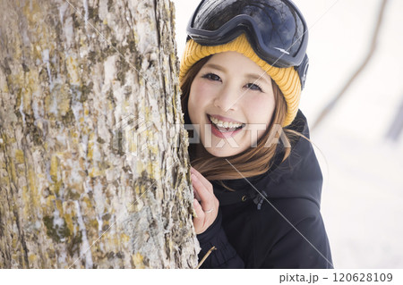 ゲレンデで木の幹から顔を出すスノボ女子 120628109