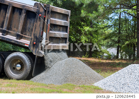 Truck unloads gravel onto grassy area preparing for landscaping work process demonstrates delivery of construction materials for improvement projects. Truck unloads gravel onto grassy area preparing for landscaping work process demonstrates delivery of construction materials for improvement projects. 120628445