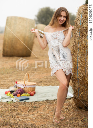 Young seductive cute girl in summer white dress standing near stack of straw enjoying holidays in countryside in field Young seductive cute girl in summer white dress standing near stack of straw enjoying holidays in countryside in field 120629078