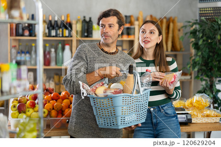 Positive couple with shopping basket walking in grocery store Positive couple with shopping basket walking in grocery store 120629204
