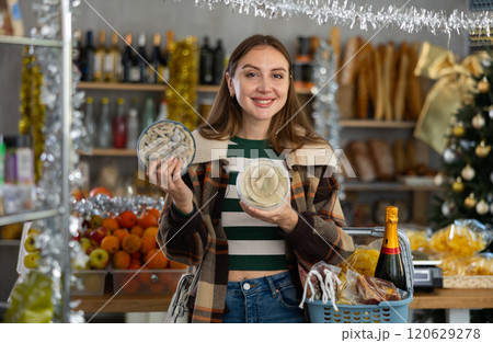 Preparing for Christmas celebration - girl chooses salted herring in produce section of supermarket Preparing for Christmas celebration - girl chooses salted herring in produce section of supermarket 120629278