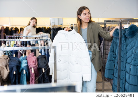 Happy girl chooses winter down jacket in clothing store Happy girl chooses winter down jacket in clothing store 120629491
