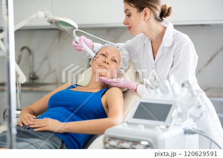Young female cosmetologist doing microcurrent procedure to adult woman Young female cosmetologist doing microcurrent procedure to adult woman 120629591