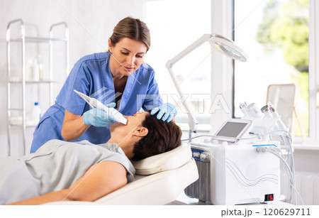 Female cosmetologist performing facial skin cleansing with ultrasonic shovel on woman 120629711