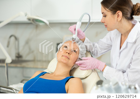 Happy adult woman getting facial deep hydration procedure from experienced cosmetologist in medicine office. Concept of professional cosmetology and rejuvenation Happy adult woman getting facial deep hydration procedure from experienced cosmetologist in medicine office. Concept of professional cosmetology and rejuvenation 120629714