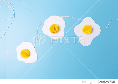 three fried eggs paper craft hanging from a string on a blue background, easter decoration concept,  120629736