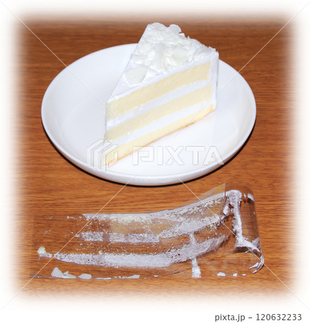 ショートケーキから剥がして折り曲げて木目調の机に置いたフィルムの内側に白いクリームが付着している状態 120632233