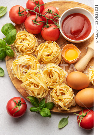 Fresh tagliatelle pasta nests with tomatoes, basil, eggs, flour and tomato sauce on wooden board Fresh tagliatelle pasta nests with tomatoes, basil, eggs, flour and tomato sauce on wooden board 120632831