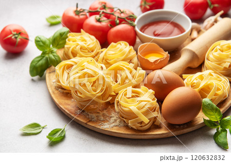 Fresh tagliatelle pasta nests with tomatoes, basil, eggs, flour and tomato sauce on wooden board 120632832