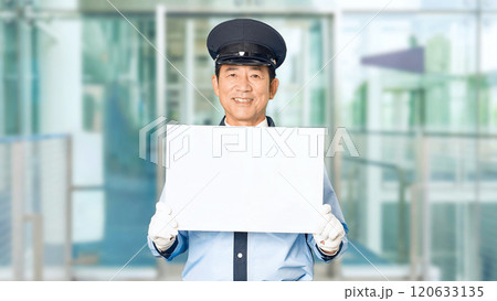 ビルのエントランスでメッセージボードを見せる男性警備員 120633135