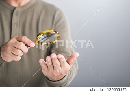 Man uses a magnifying glass to examine his palm, reflecting the practice of palmistry to enhance luck and fate. Represents the widespread belief in fortune-telling through palm readings in Thailand 120633173