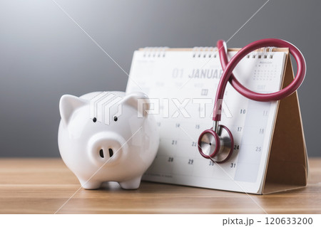 White piggy bank, a calendar, and a stethoscope on a table symbolize financial health, planning, and the importance of balancing savings with medical preparedness 120633200