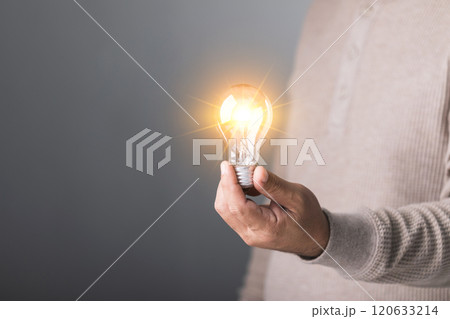 A man holds a clear light bulb, symbolizing the spark of new ideas and creativity. This image represents innovation, inspiration, and the power of fresh thinking A man holds a clear light bulb, symbolizing the spark of new ideas and creativity. This image represents innovation, inspiration, and the power of fresh thinking 120633214