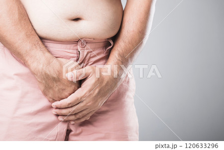 Man with excess weight stands, holding his waistband, indicating potential urinary issues linked to obesity. Highlights the connection between weight-related health problems and men's well-being 120633296
