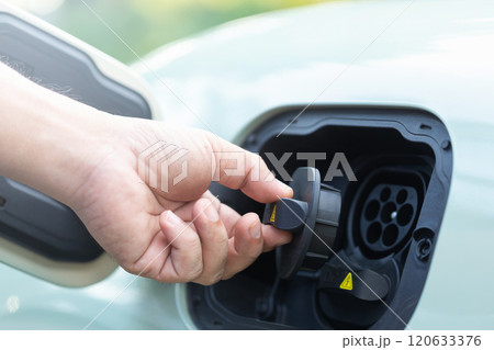 Car owner's hand grips the rubber cap of an electric vehicle charger, preparing to open or close it after use. Proper handling and maintenance in the use of clean energy charging solutions 120633376