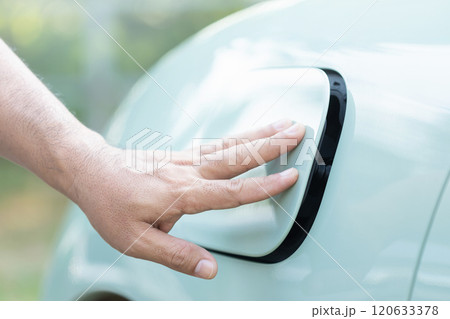 A car owner's hand gently touches the charging port cover of an electric vehicle, either opening or closing it after charging. Importance of proper handling in electric vehicle maintenance A car owner's hand gently touches the charging port cover of an electric vehicle, either opening or closing it after charging. Importance of proper handling in electric vehicle maintenance 120633378