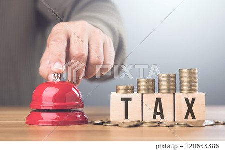 Hand presses a red bell beside a stack of coins on a wooden block labeled TAX, An urgent call to address tax matters and financial planning, Timely tax payments and financial responsibility 120633386