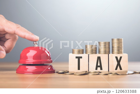 Hand presses a red bell beside a stack of coins on a wooden block labeled TAX, An urgent call to address tax matters and financial planning, Timely tax payments and financial responsibility 120633388