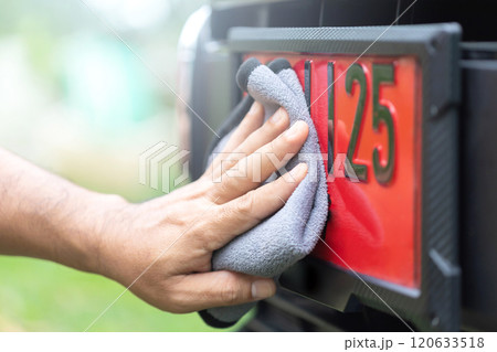 Car owner carefully cleans a red license plate, used for new cars before registration, reflecting Thai beliefs in lucky numbers and the importance of maintaining auspicious symbols for good fortune 120633518