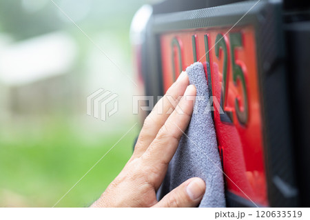 Car owner carefully cleans a red license plate, used for new cars before registration, reflecting Thai beliefs in lucky numbers and the importance of maintaining auspicious symbols for good fortune 120633519