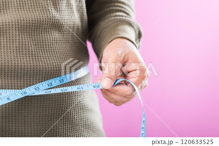 Man measuring his waistline with a tape measure, emphasizing the importance of regular health checks and awareness of weight management to promote better overall health Man measuring his waistline with a tape measure, emphasizing the importance of regular health checks and awareness of weight management to promote better overall health 120633525
